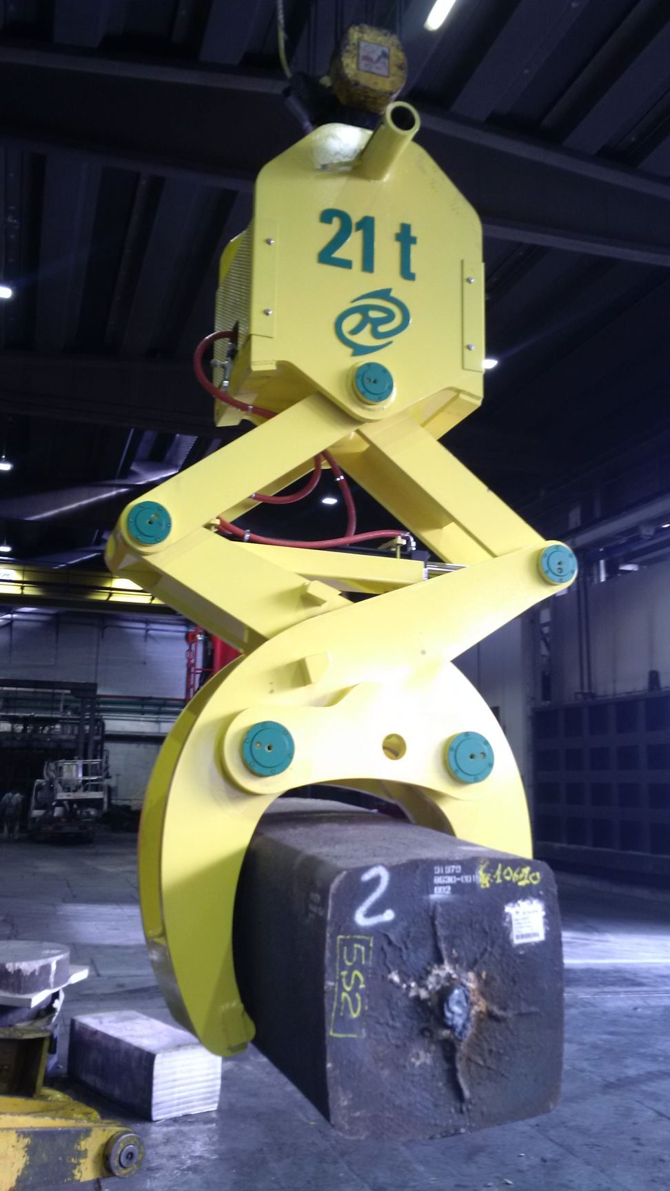 Dispositivo di sollevamento industriale giallo che sostiene un grande blocco di metallo nero all'interno; etichetta 