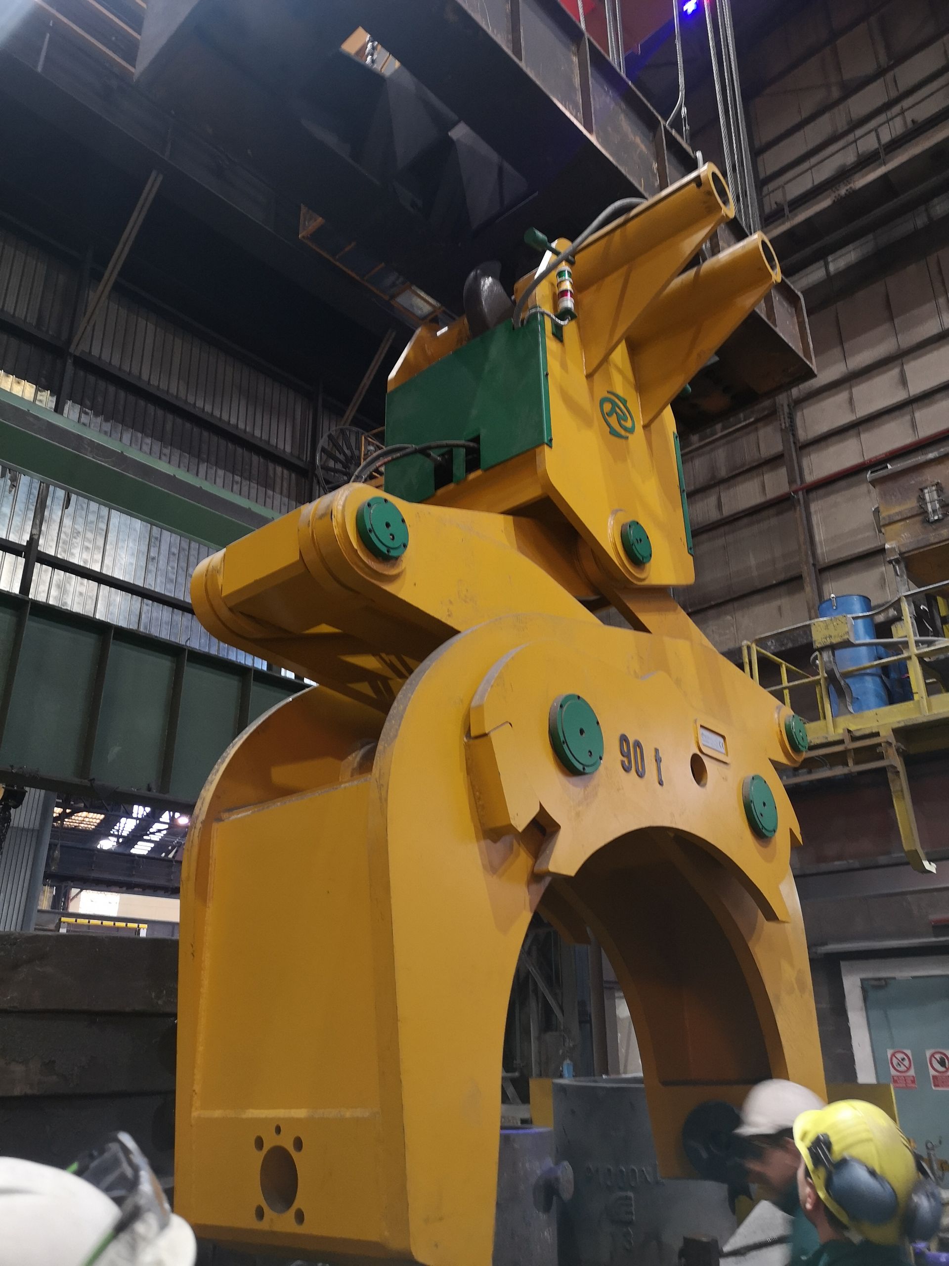 Grande pinza industriale gialla sospesa a una gru, in un ambiente industriale.