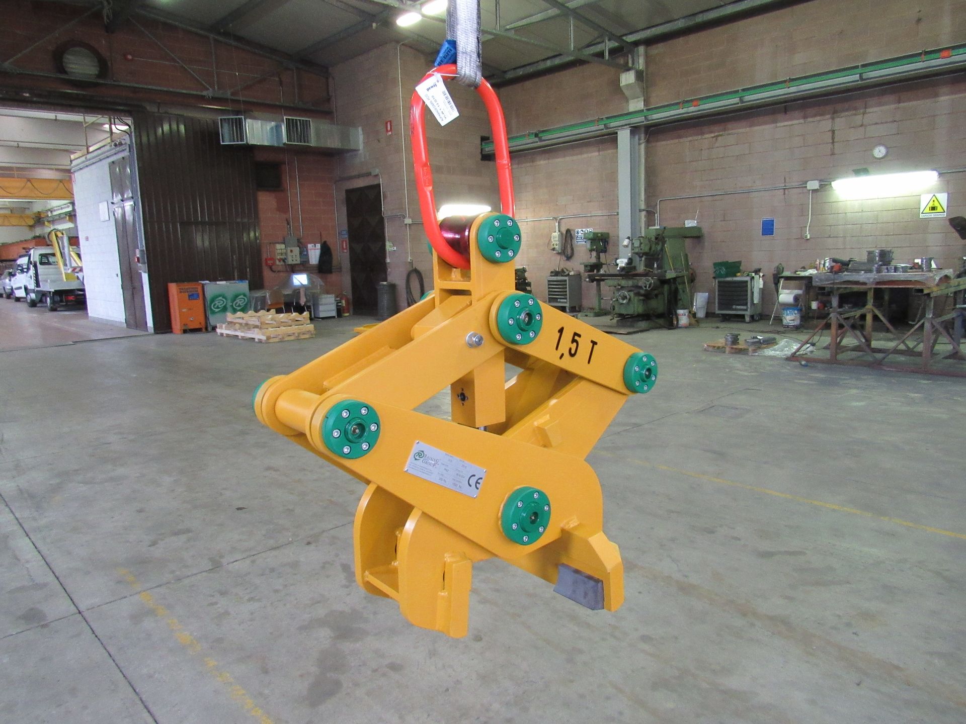 Pinza di sollevamento gialla sospesa a un'imbracatura rossa e bianca in un magazzino.