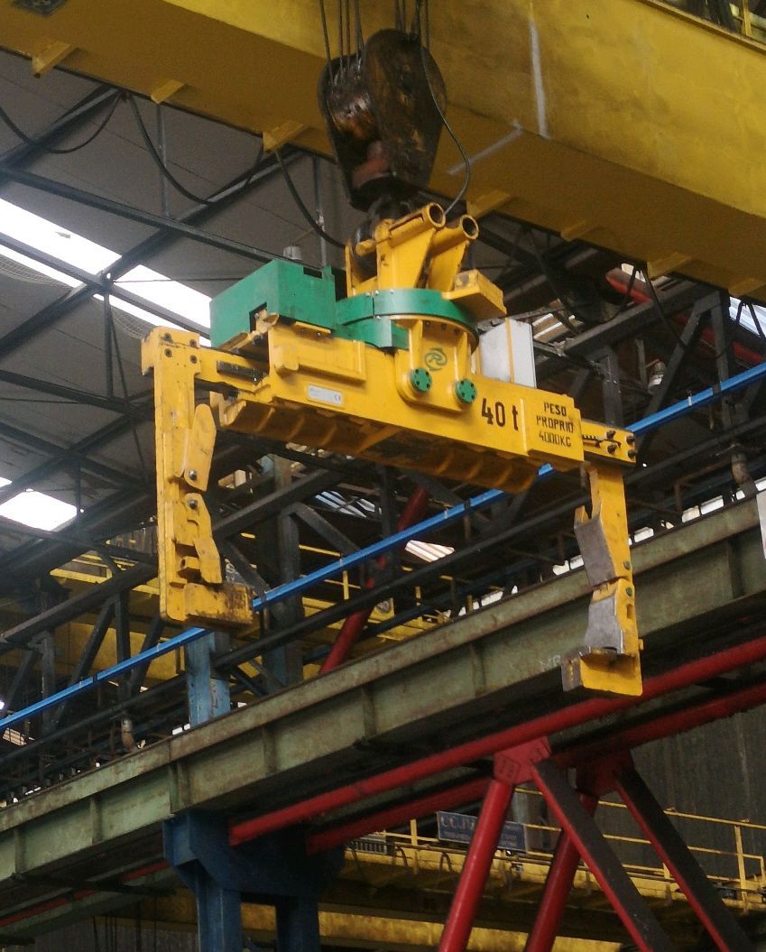 Gru industriale gialla che solleva un carico pesante. Travi e strutture in acciaio in un magazzino.