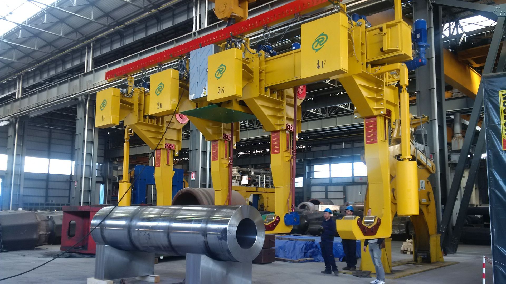 Sistema di gru a portale giallo che solleva una grande bobina di metallo in un ambiente di fabbrica.