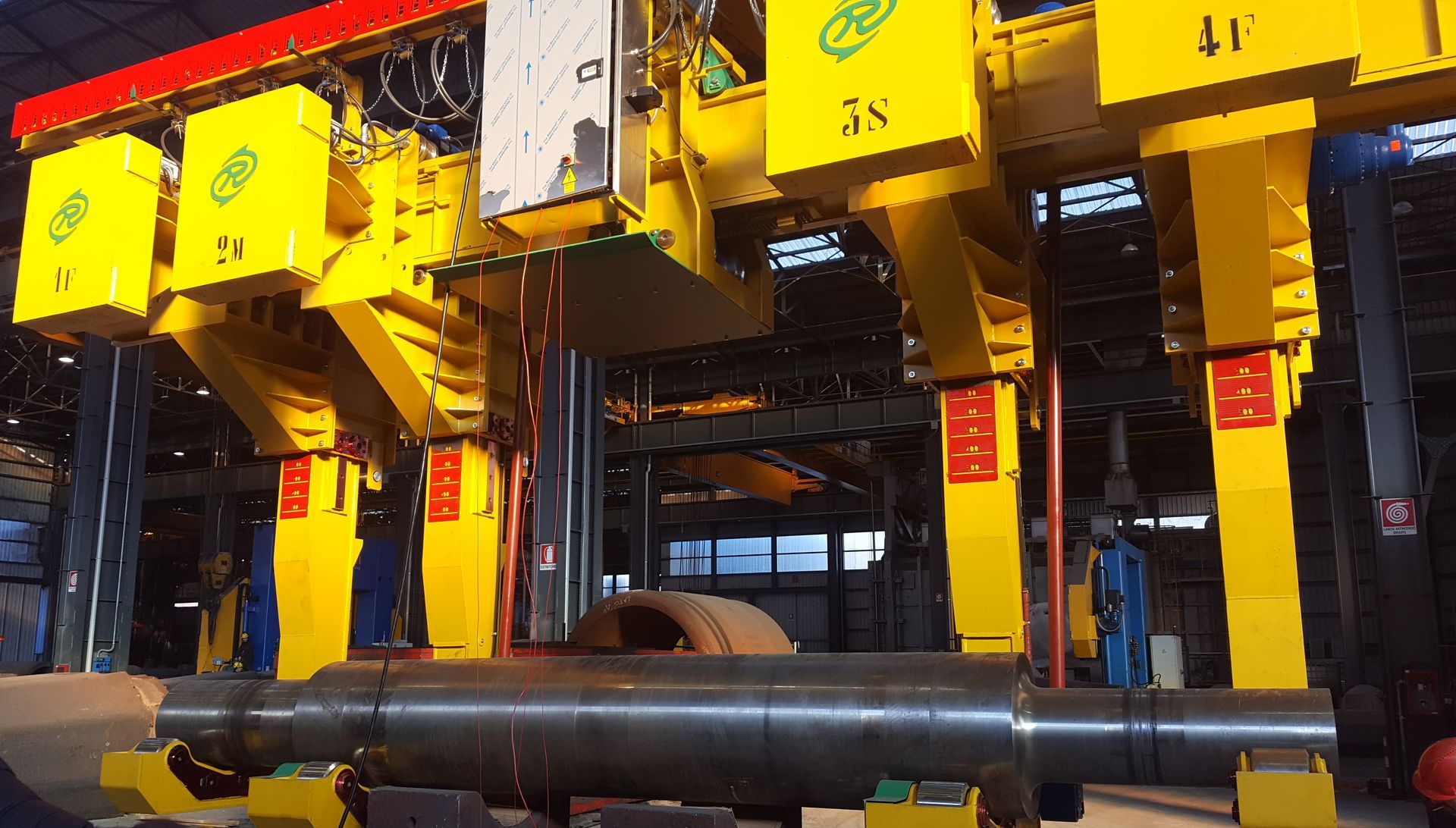 Grande macchina industriale gialla sopra un albero metallico in un ambiente di fabbrica.