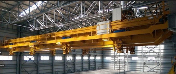 Gru a ponte gialla all'interno di un magazzino. Travi in ​​acciaio formano il tetto e la struttura di supporto.