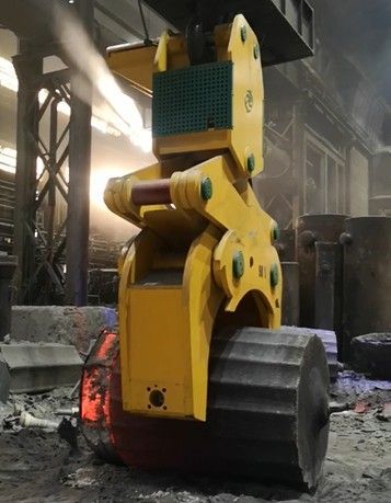 Macchina industriale gialla che solleva un oggetto metallico rovente in una fabbrica. Il vapore sale.