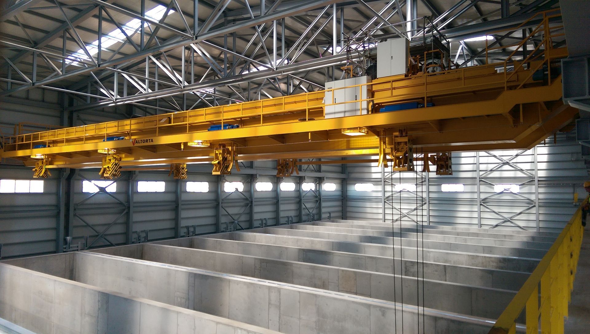 Gru industriale gialla sopra le vasche di cemento in un magazzino.