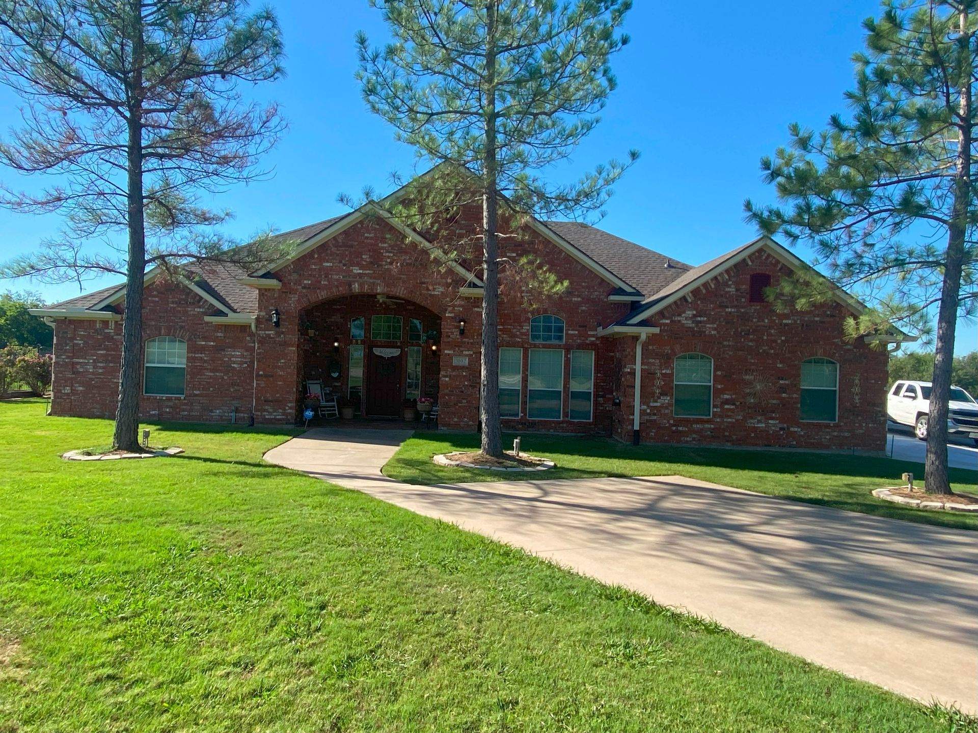 A large brick house with a driveway and trees in front of it.