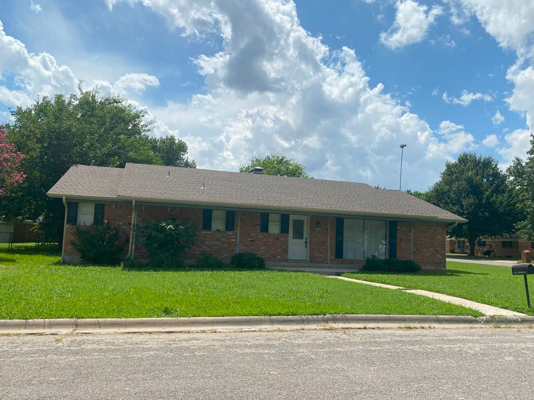 A brick house with a gray roof is sitting on top of a lush green lawn.