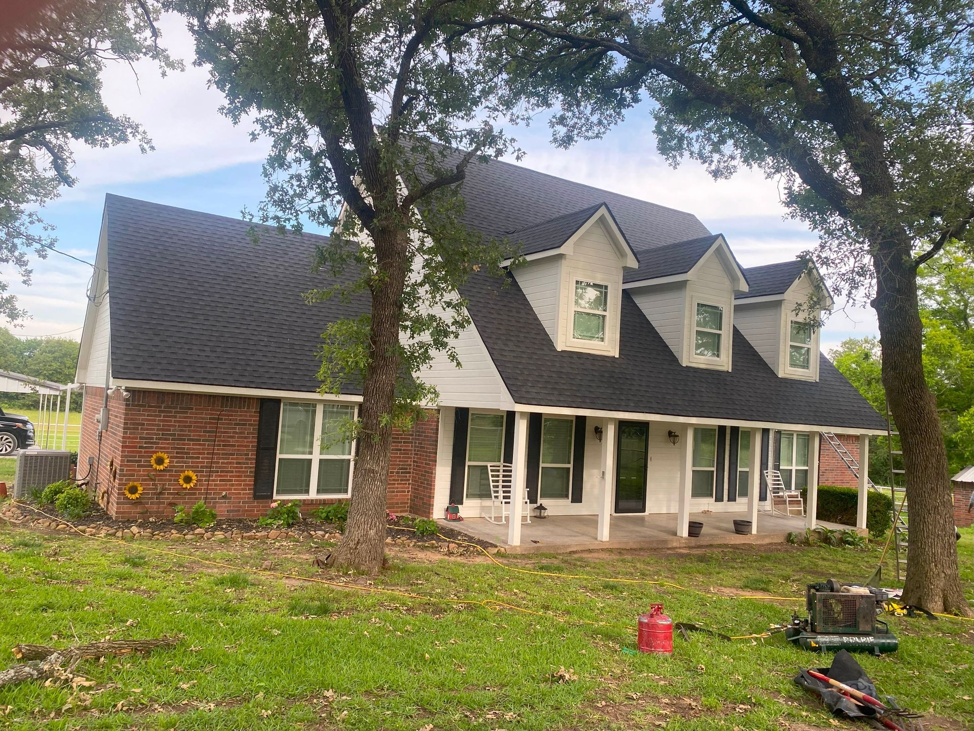 A large brick house with a black roof is sitting on top of a lush green field.