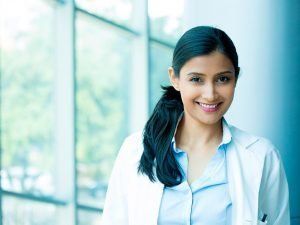 A woman in a lab coat is smiling in front of a window.