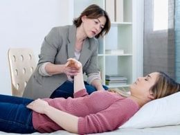 A woman is laying on a bed talking to another woman.