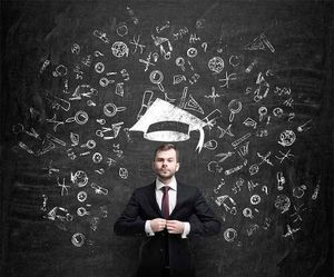 A man in a suit and tie is standing in front of a blackboard with a graduation cap on his head.