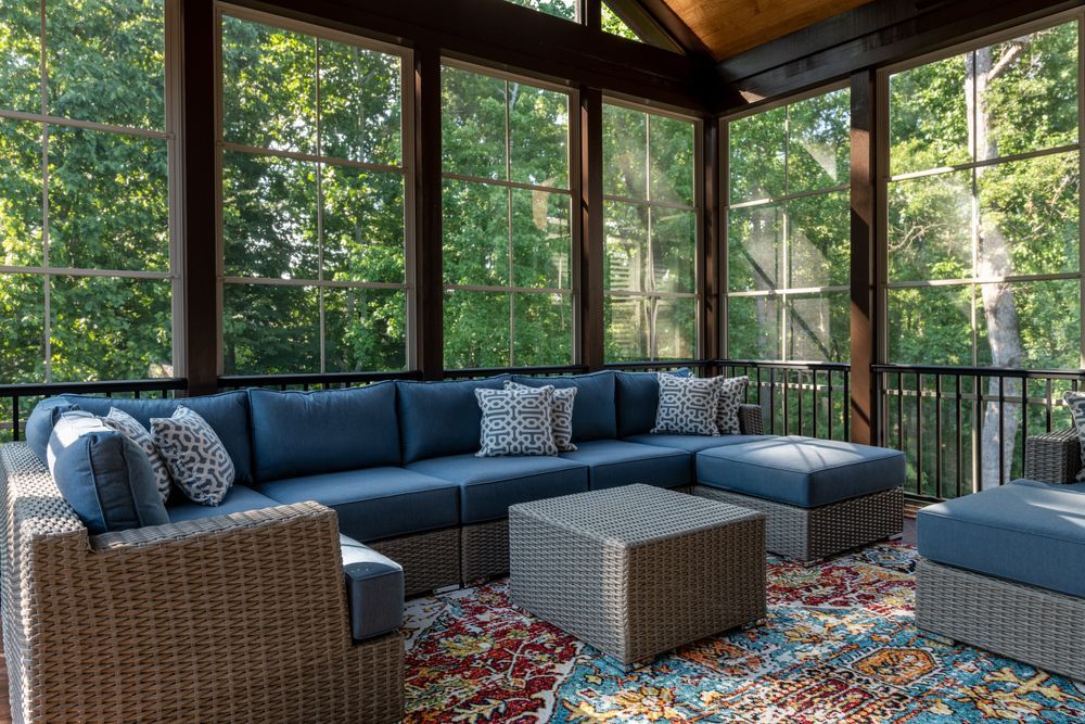 A screened in porch with wicker furniture and a rug.