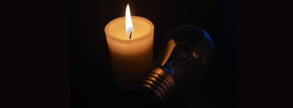 A candle is lit next to a light bulb in the dark.