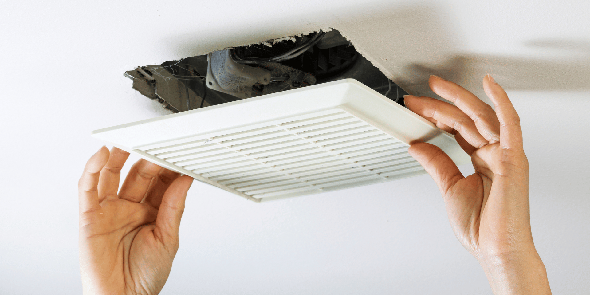 Hands holding a white vent cover up to a black, dirty vent opening.