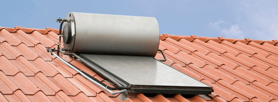 Solar water heater on a red tiled roof against a blue sky.