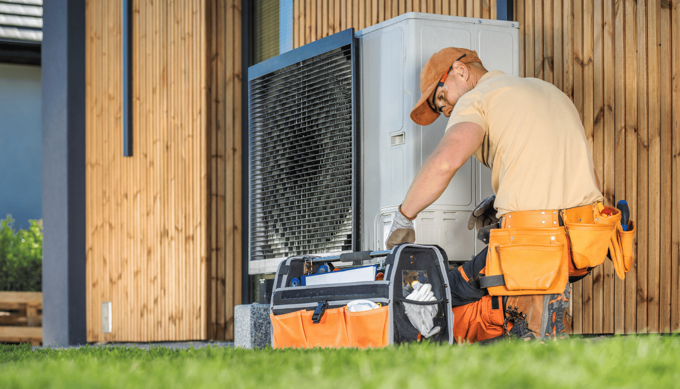 A man is working on a heat pump outside of a house.