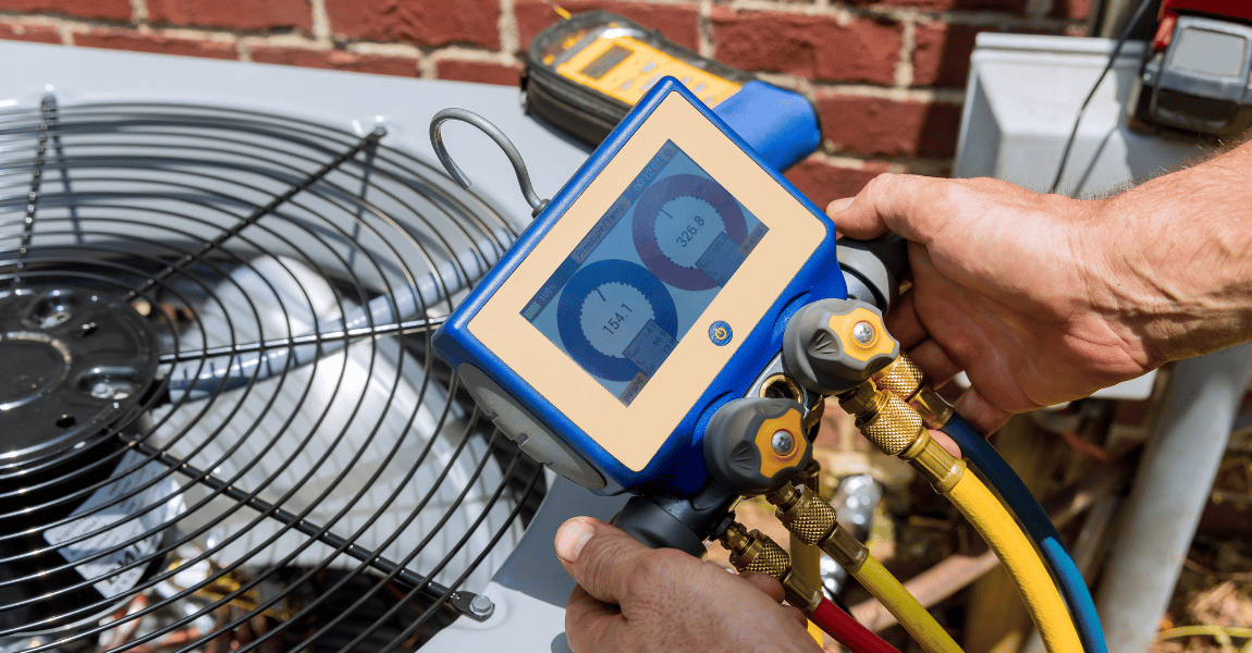 A man is holding a digital gauge in front of an air conditioner.