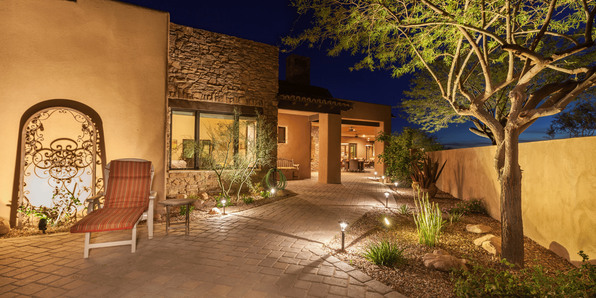 A home exterior lit at night with a courtyard and a tree.
