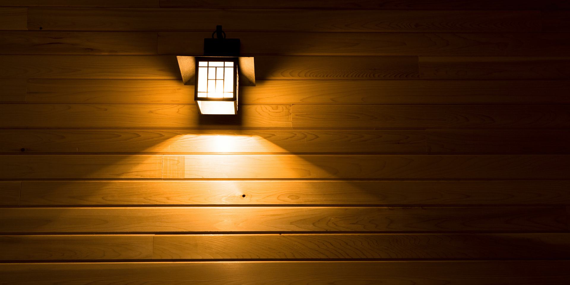A lit wall sconce casts a warm glow on a wooden wall.