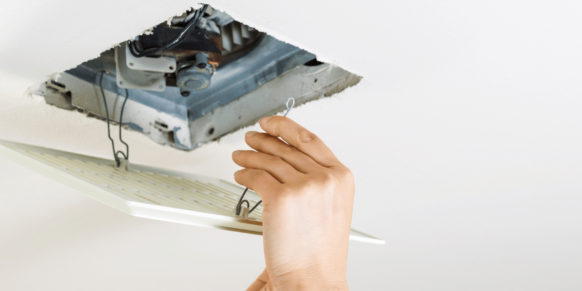 Person's hand removing the cover of a ceiling vent to reveal internal components.