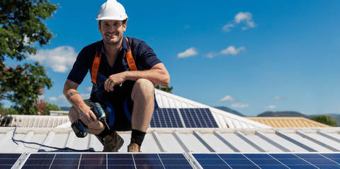 A man is kneeling on top of a roof with solar panels.
