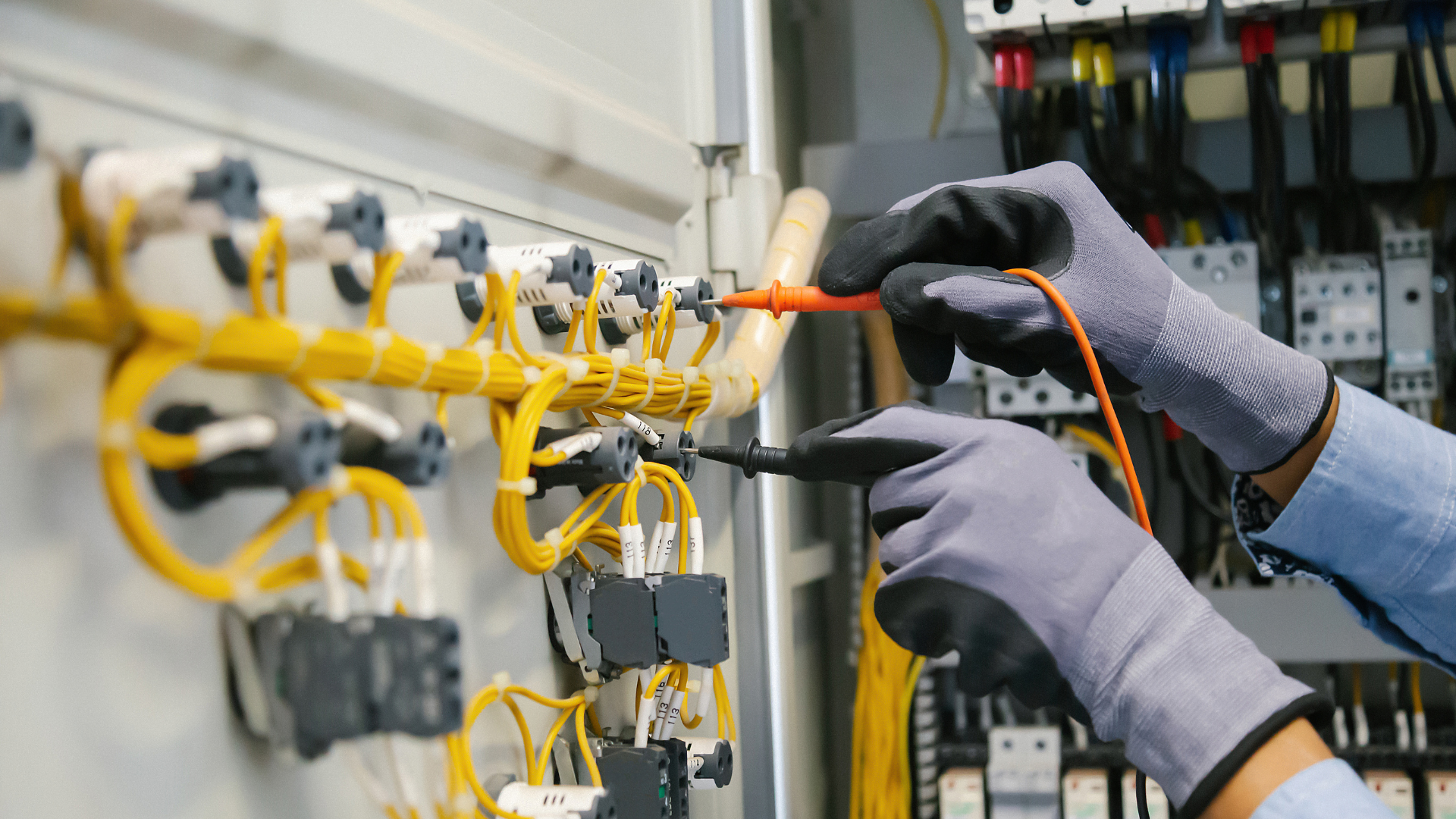 An electrician is working on an electrical panel with a multimeter.