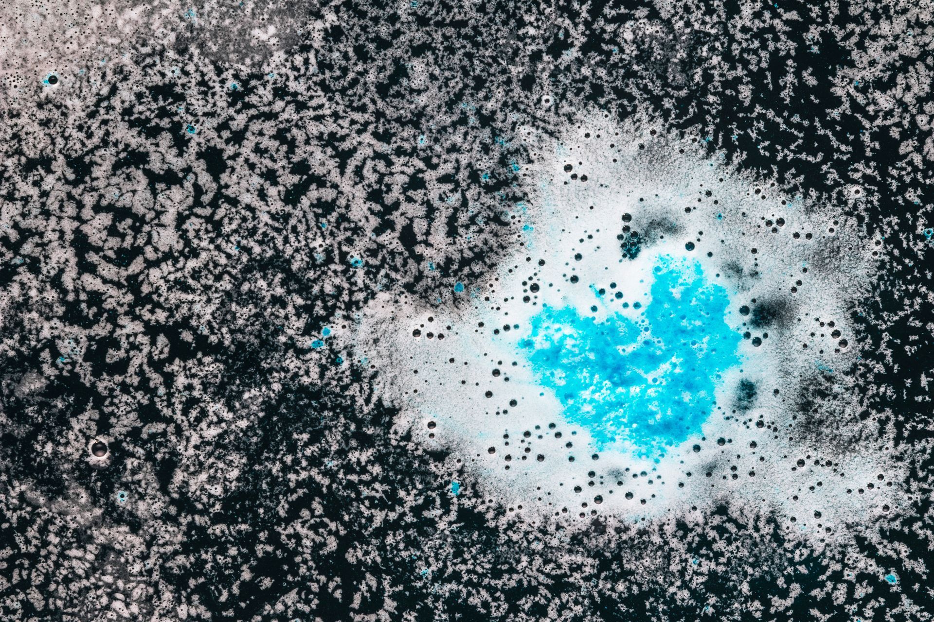 Flores de tela de colores en un jarrón con una vela encendida sobre un posavasos de piedra.