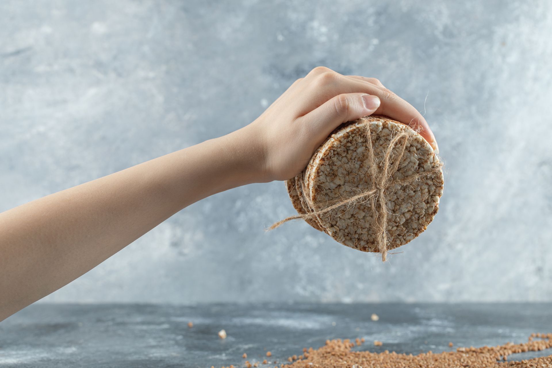Mano sosteniendo una pila de galletas redondas y granulosas atadas con cordel sobre un fondo azul grisáceo.