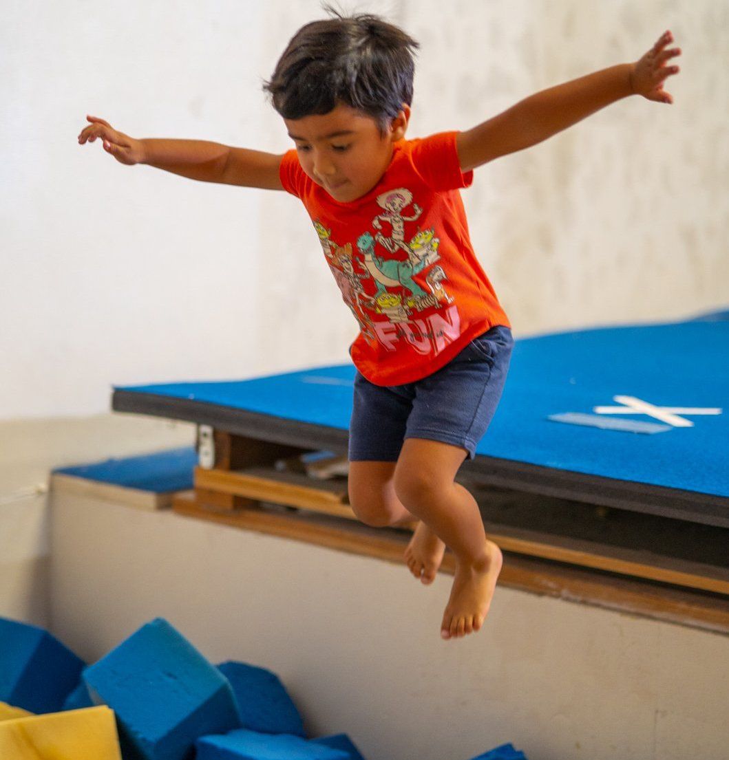 A young boy in an orange shirt is jumping in the air