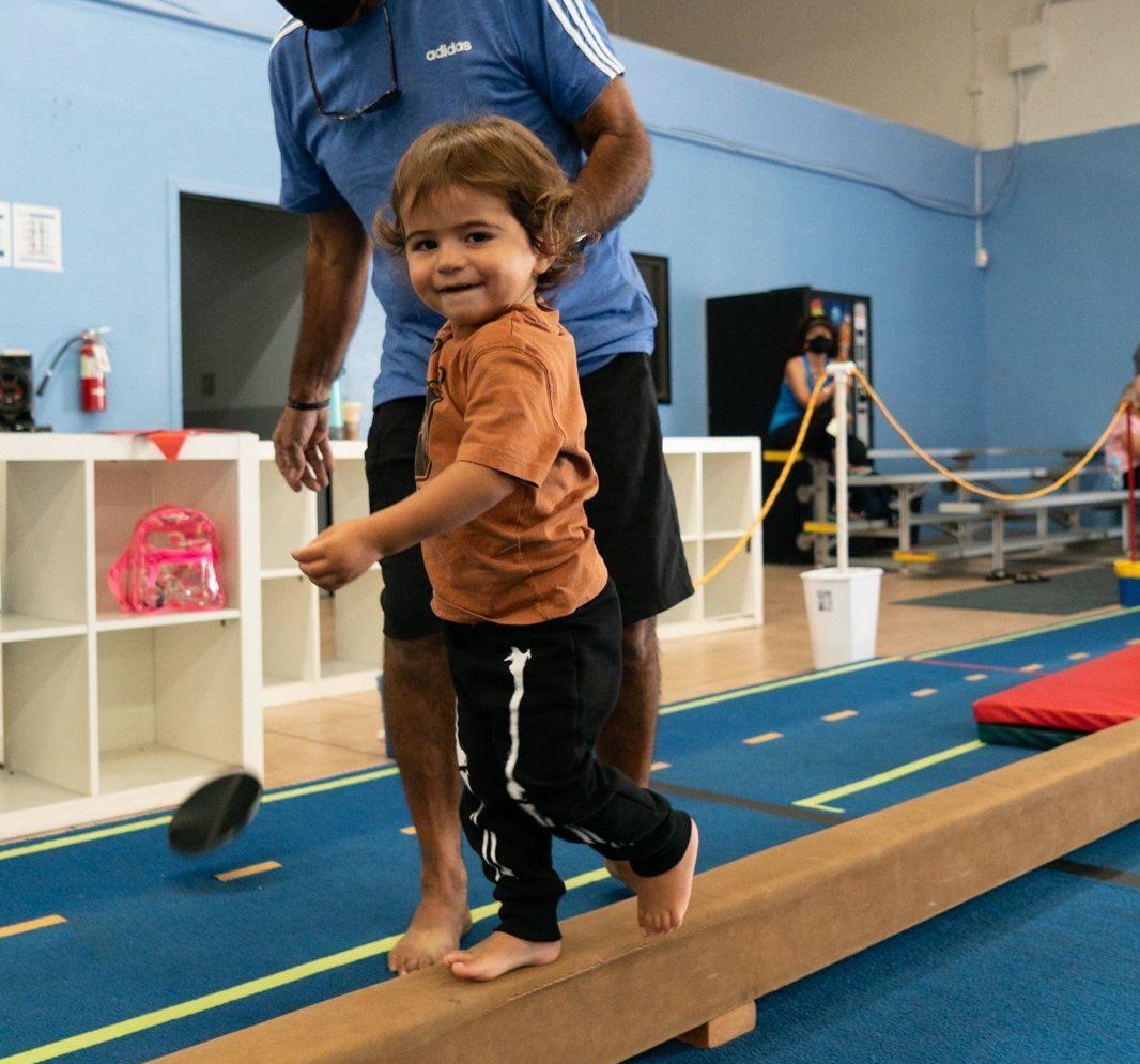 A man helps a little boy walk on a balance beam