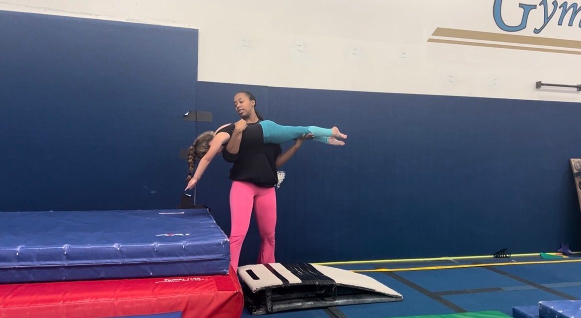 A young girl is doing a split on the floor in a gym.