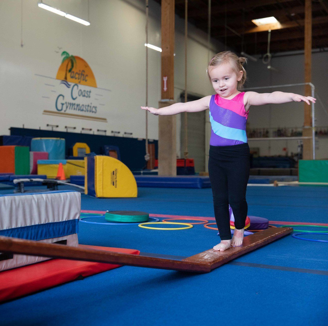 A little girl is sitting on a yoga mat stretching her legs.