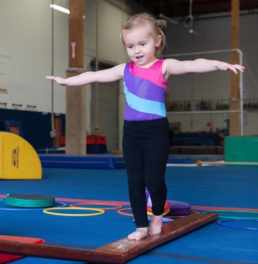 A little girl is standing on a balance beam in a gym