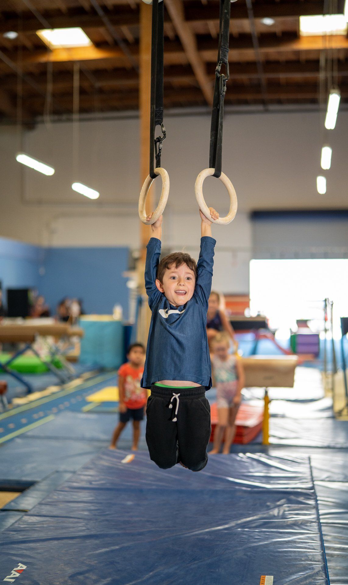 A young boy is hanging from a pair of rings in a gym.