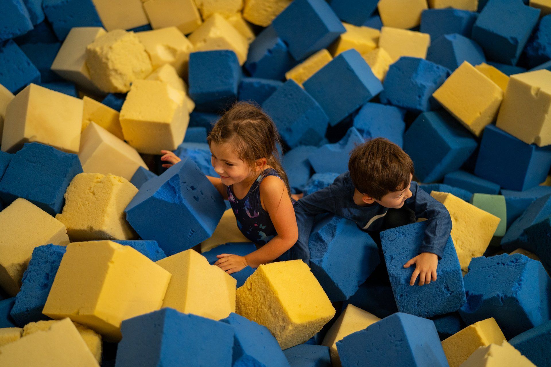 A boy and a girl are playing in a pile of foam cubes.