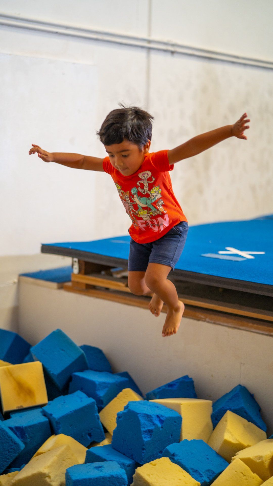 A young boy is jumping in a pool of foam cubes.