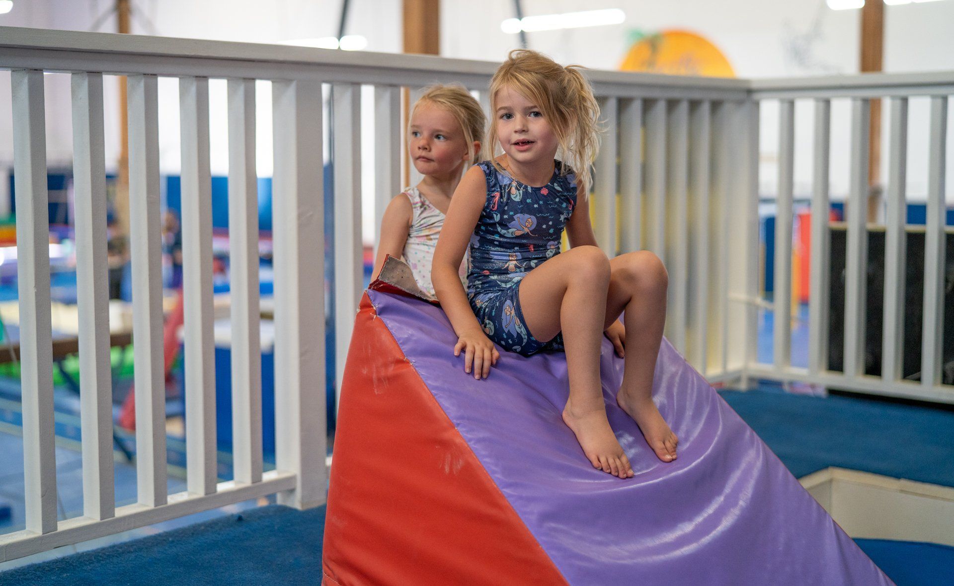 Two little girls are sitting on a purple and red mat.