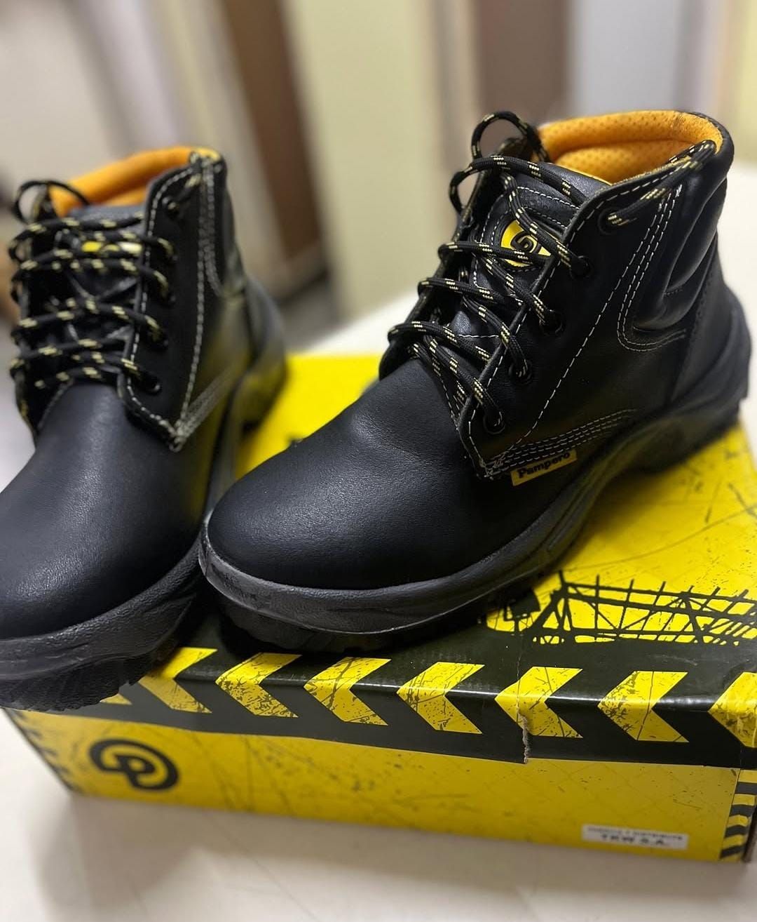 Botas de trabajo negras con cordones amarillos sobre una caja amarilla con franjas negras de advertencia.
