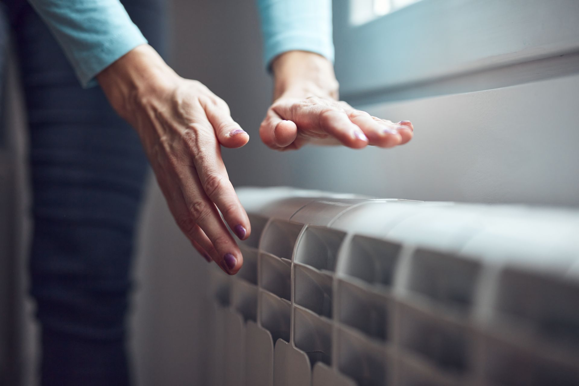 Hands hovering over a white radiator, checking its heat.