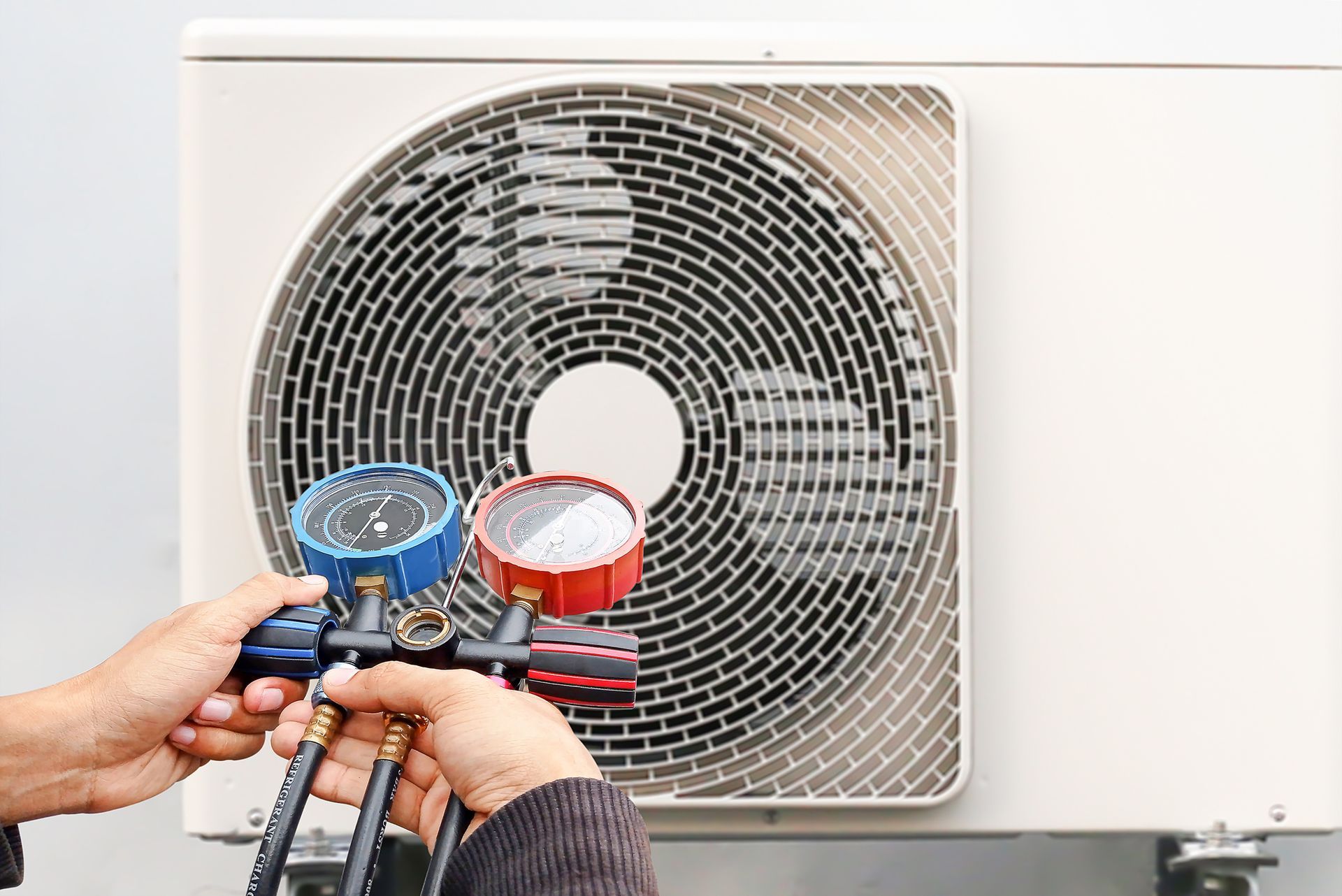 HVAC technician checking AC unit with manifold gauge for maintenance.