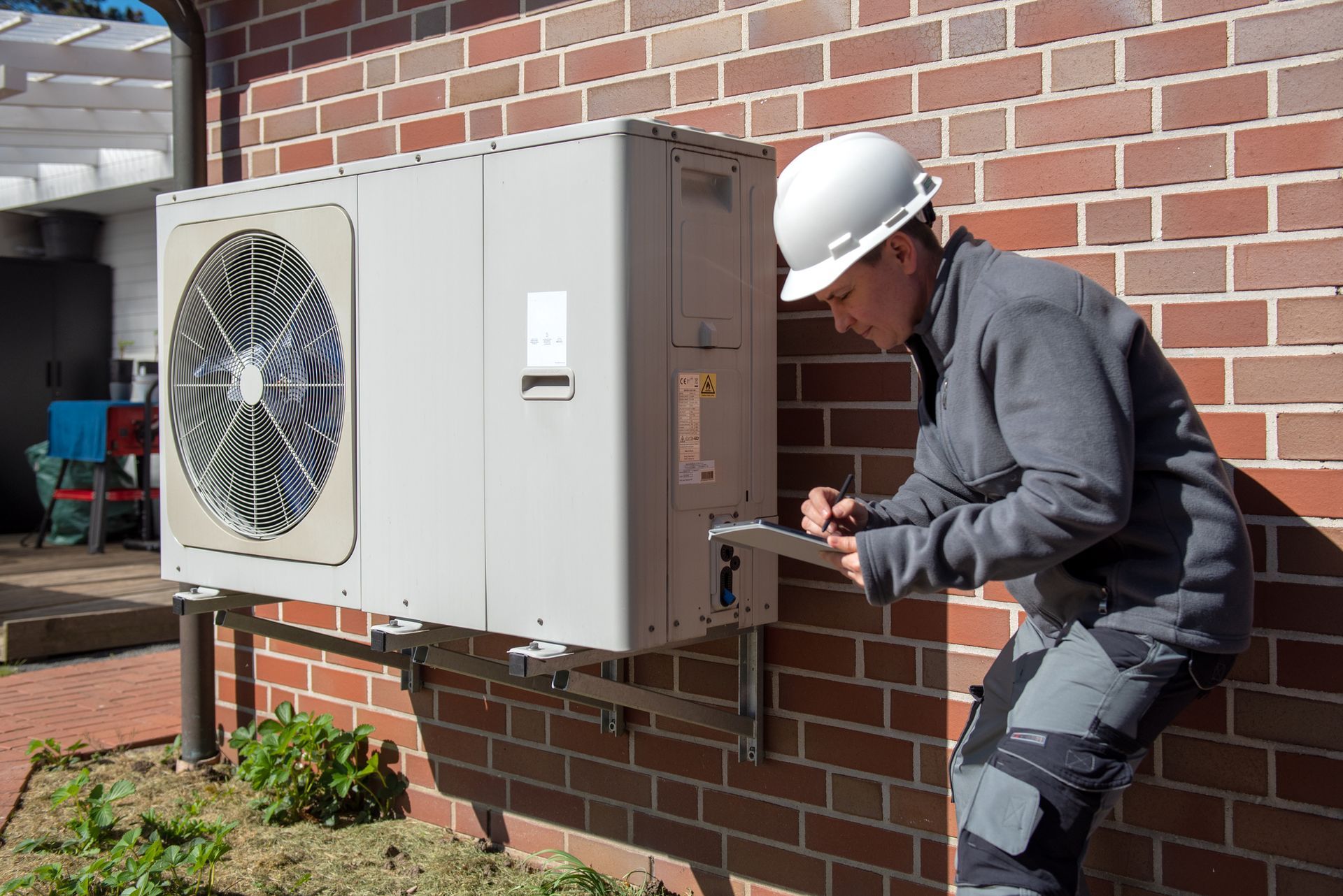 HVAC repairman taking notes about a HVAC system outside a property, using white helmet.