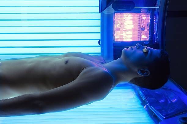 A shirtless man is laying in a tanning bed.