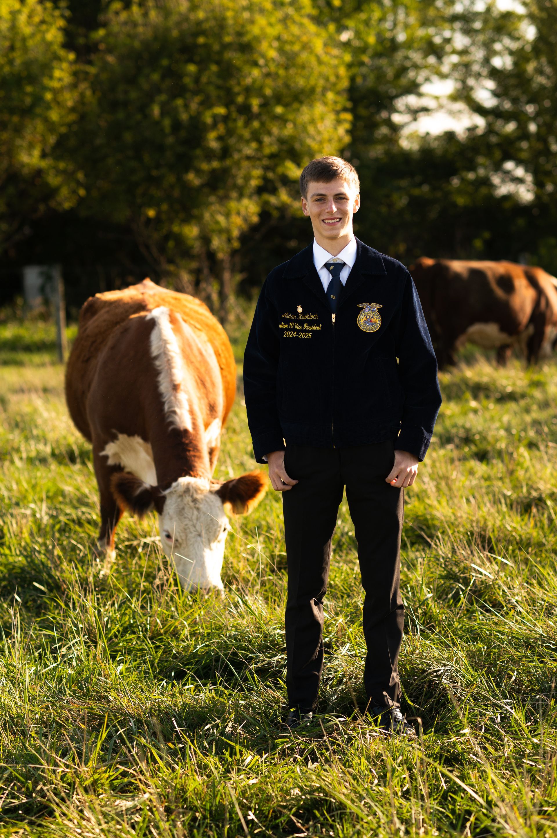 aidan knobloch outside in ffa jacket next to livestock