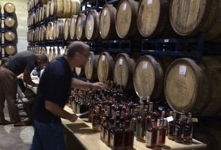 A man is pouring a bottle of whiskey into a barrel