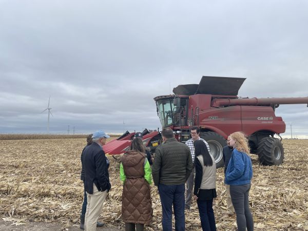 A group of people are standing in a field looking at a combine harvester.