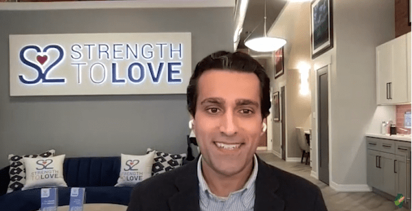 A man is smiling in front of a sign that says strength to love.