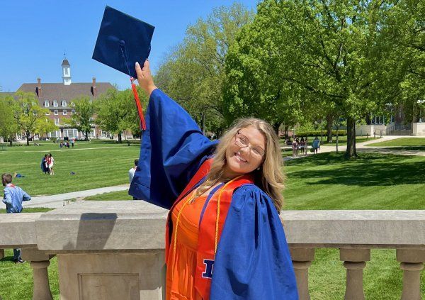 A woman in a graduation cap and gown is holding her cap in the air.