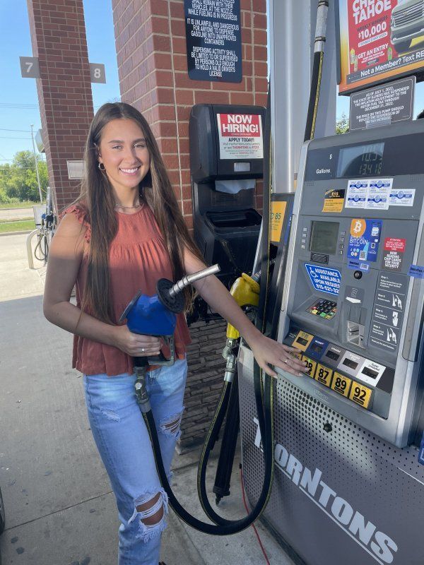 A woman is pumping gas into a gas pump at a gas station.