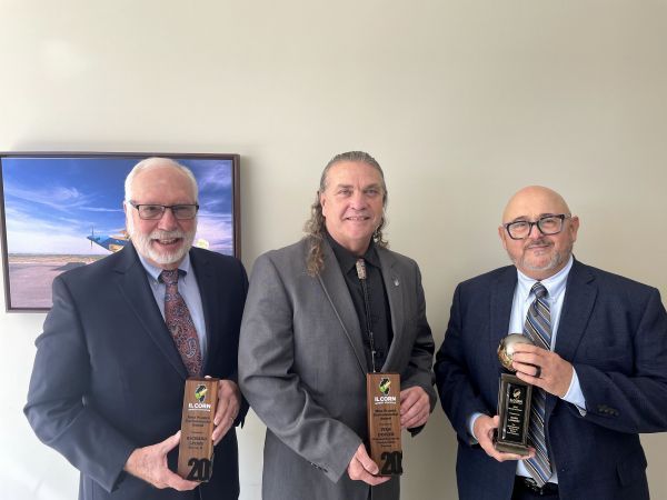 Three men in suits and ties are holding awards