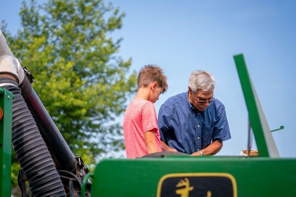 A man and a boy are looking at a green john deere tractor.